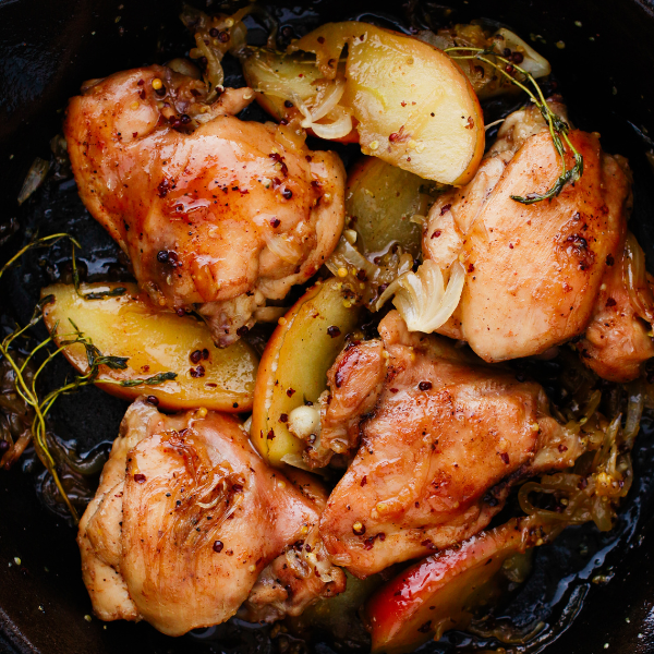 Juicy chicken thighs and apple slices simmered in a rich apple cider sauce inside a black skillet.