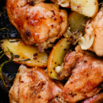 Juicy chicken thighs and apple slices simmered in a rich apple cider sauce inside a black skillet.