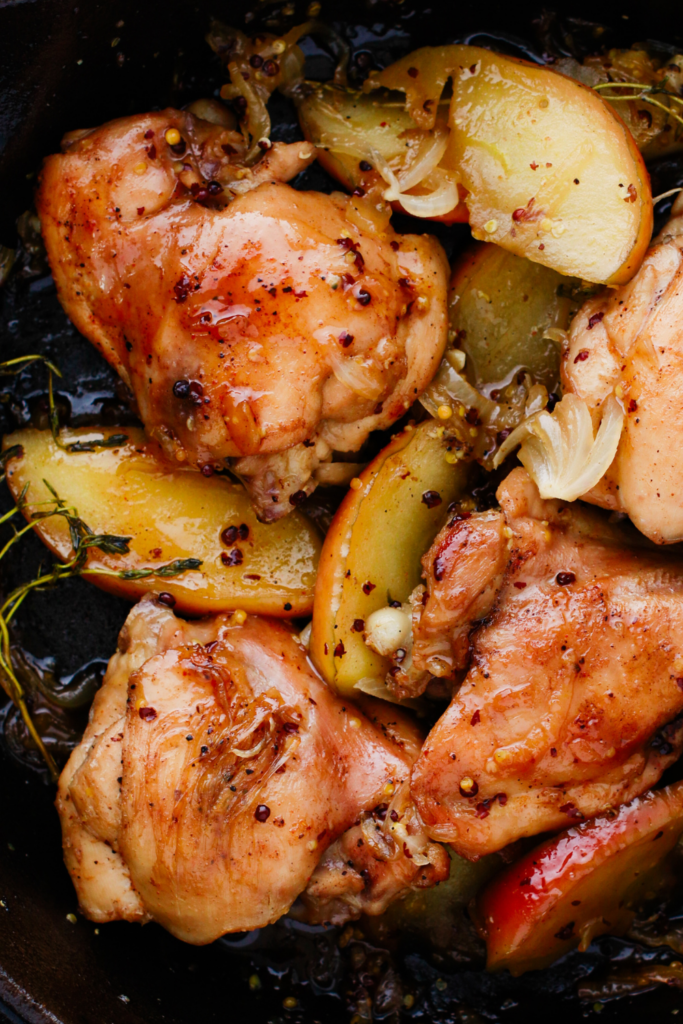 Juicy chicken thighs and apple slices simmered in a rich apple cider sauce inside a black skillet.