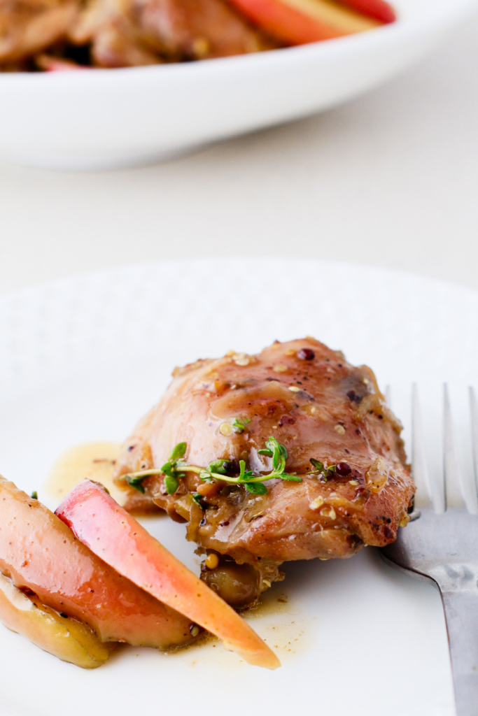 A serving of apple cider chicken thigh on a white plate with tender apple slices and a drizzle of savory sauce.