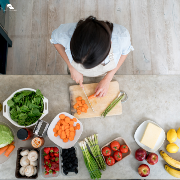 A woman chopping carrots in a bright kitchen surrounded by fresh produce, illustrating a homemaking goal of healthy meal planning for a happier home in 2026.