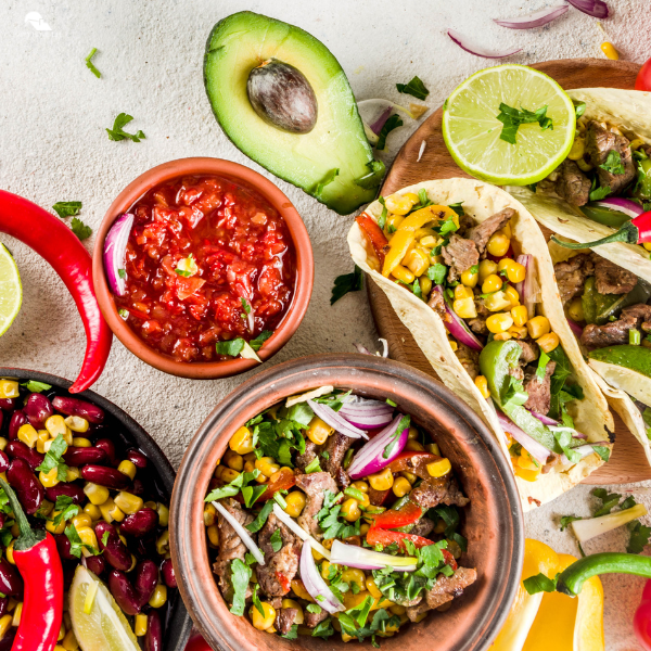 Festive spread of tacos, fresh salsa, avocado, beans, corn, and lime representing recipes from a collection of Cinco de Mayo recipes.